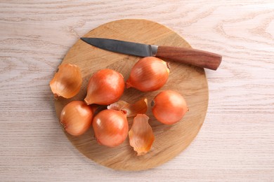 Photo of Tray with ripe onions and knife on wooden table, top view