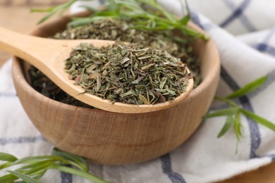 Photo of Bowl of dry tarragon and spoon on wooden table, closeup
