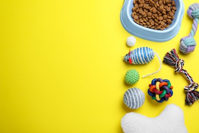 Photo of Feeding bowl and toys for pet on yellow background, flat lay. Space for text