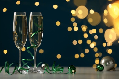 Glasses of champagne with serpentine streamers and Christmas balls on table against blurred lights. Space for text