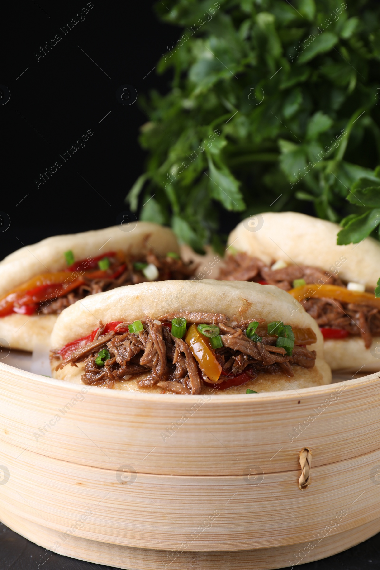 Photo of Delicious gua bao in bamboo steamer on black table, closeup