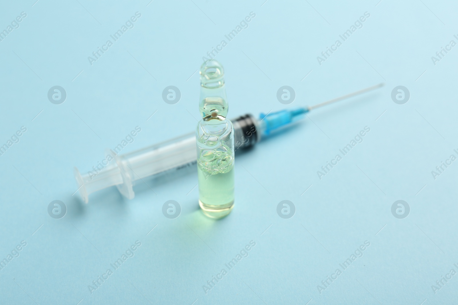 Photo of Glass ampoule with liquid and syringe on light blue background, closeup