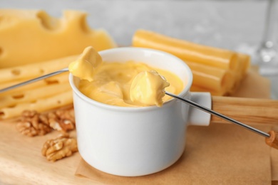 Photo of Pot of tasty cheese fondue and fork with bread on cutting board