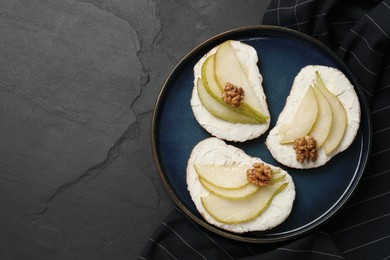 Delicious bruschettas with ricotta cheese, pears and walnuts on dark textured table, top view. Space for text