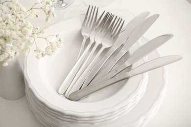 Photo of Stacked plates with cutlery on white table, closeup