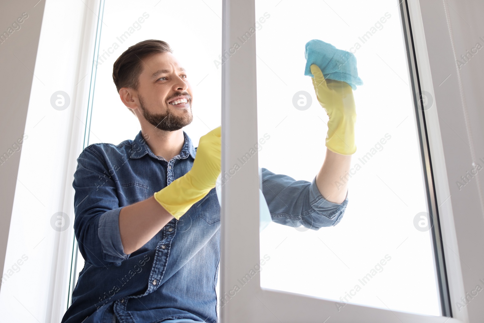 Photo of Man in casual clothes washing window glass at home