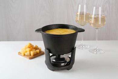 Photo of Fondue with tasty melted cheese and aromatic wine in glasses on white table