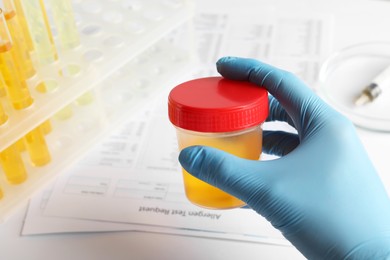 Photo of Nurse holding container with urine sample at table, closeup and space for text. Specimen collection