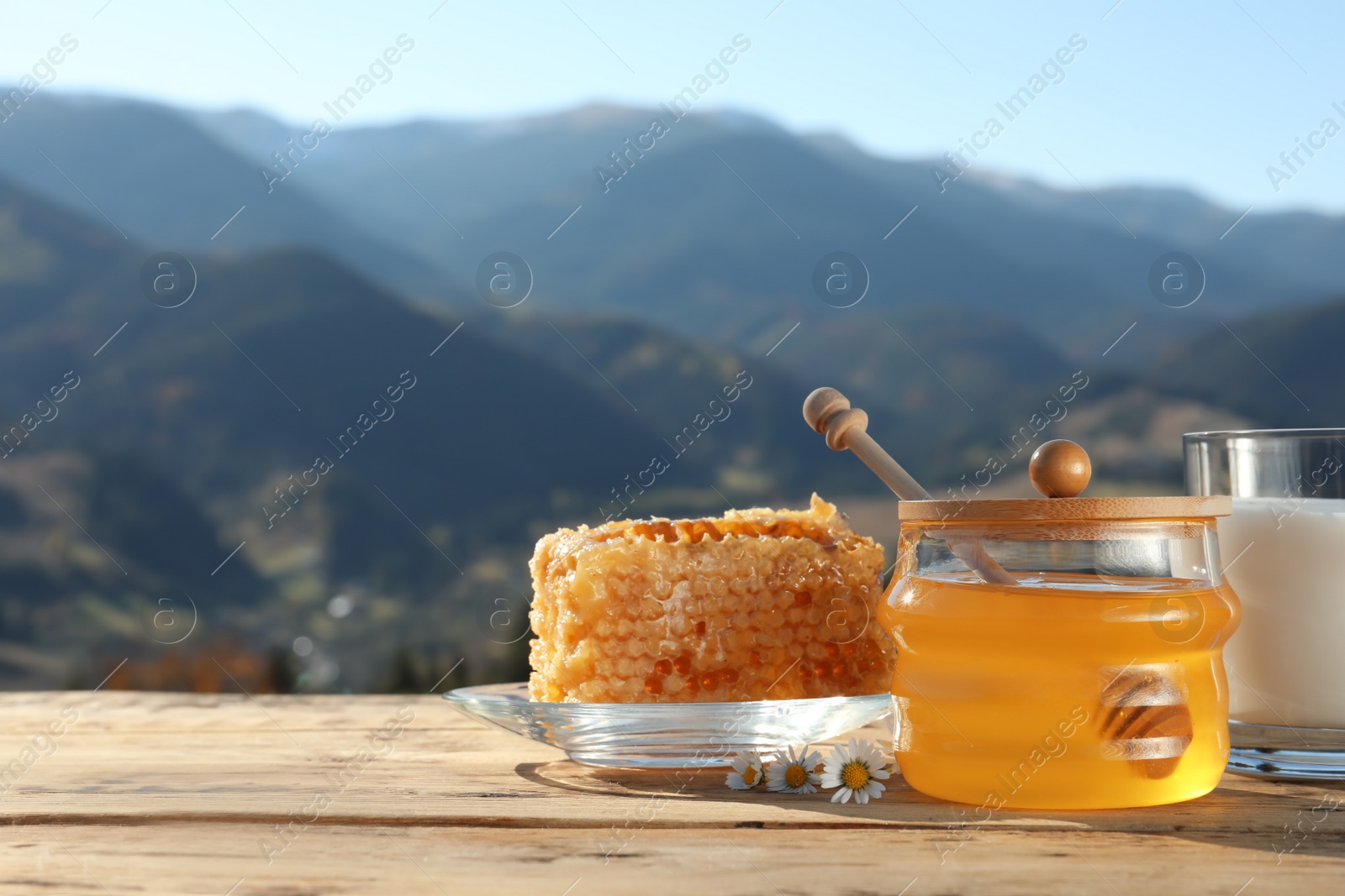 Photo of Fresh aromatic honey, combs and glass of milk on wooden table against mountain landscape. Space for text