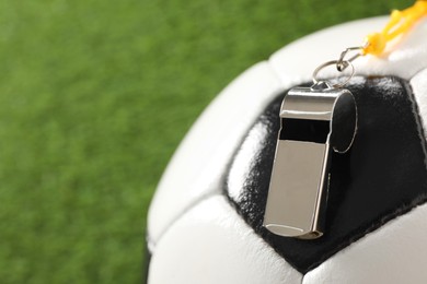 Photo of Football referee equipment. Soccer ball and metal whistle on green grass, closeup with space for text