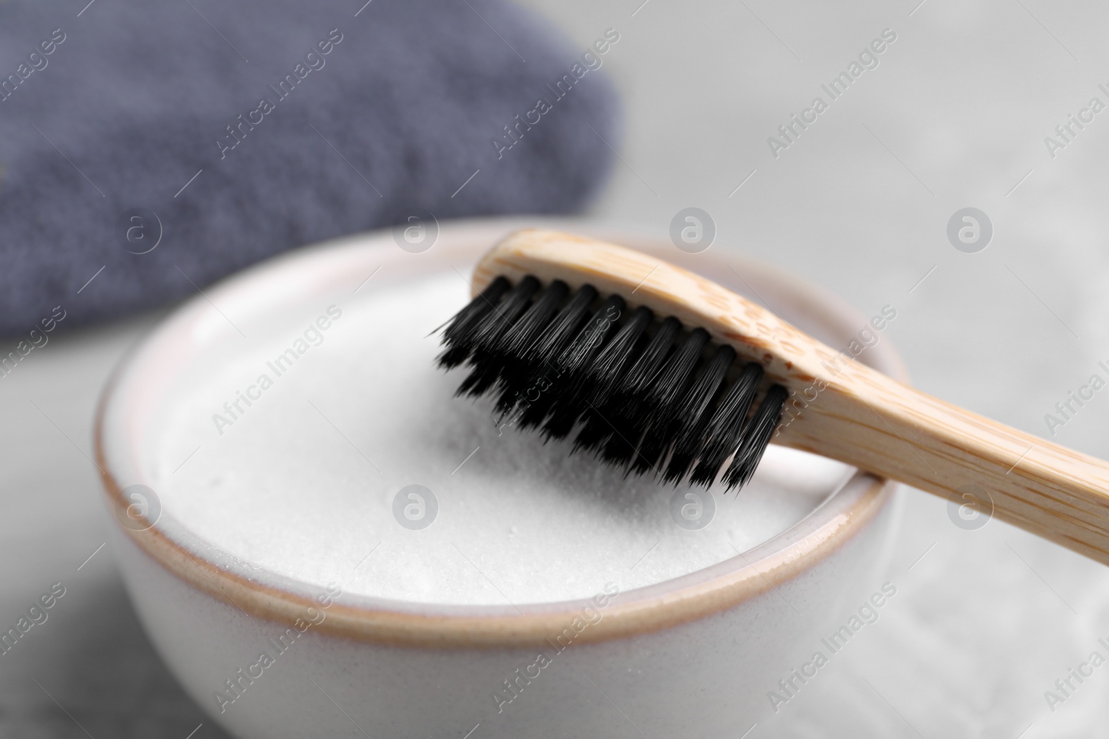 Photo of Bamboo toothbrush and bowl of baking soda on light grey table, closeup