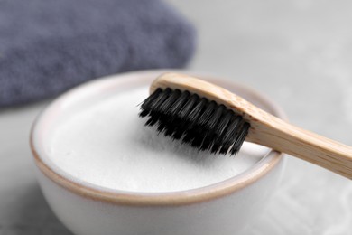 Bamboo toothbrush and bowl of baking soda on light grey table, closeup