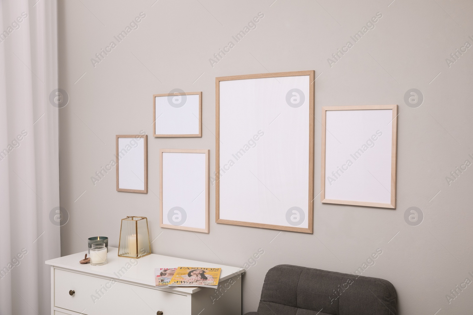 Photo of Empty frames hanging on grey wall over white chest of drawers. Mockup for design