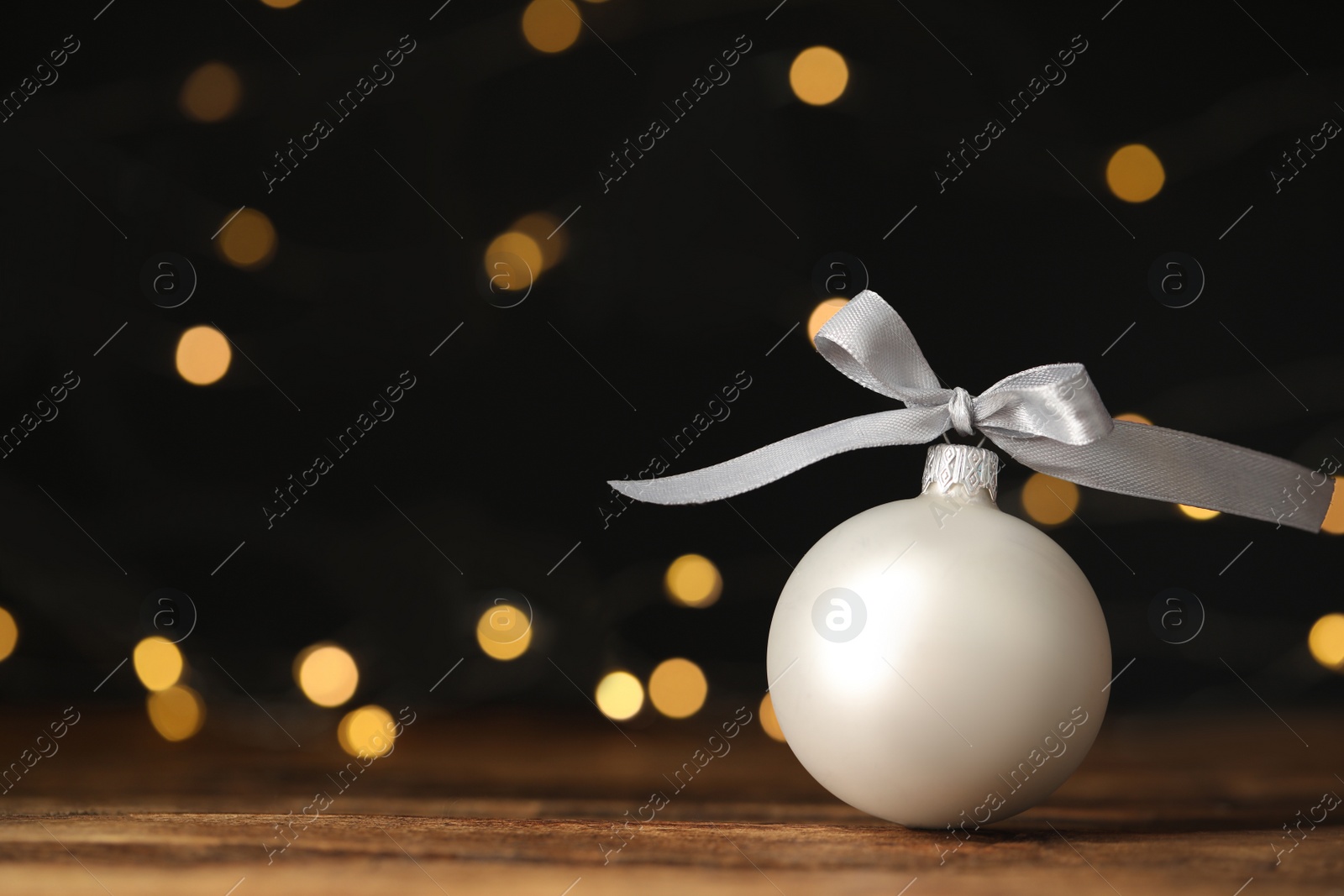 Photo of Beautiful Christmas ball on wooden table against blurred festive lights. Space for text