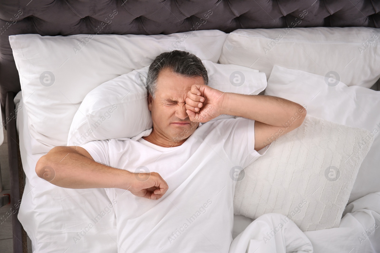 Photo of Man waking up after sleeping on comfortable pillow in bed at home, top view