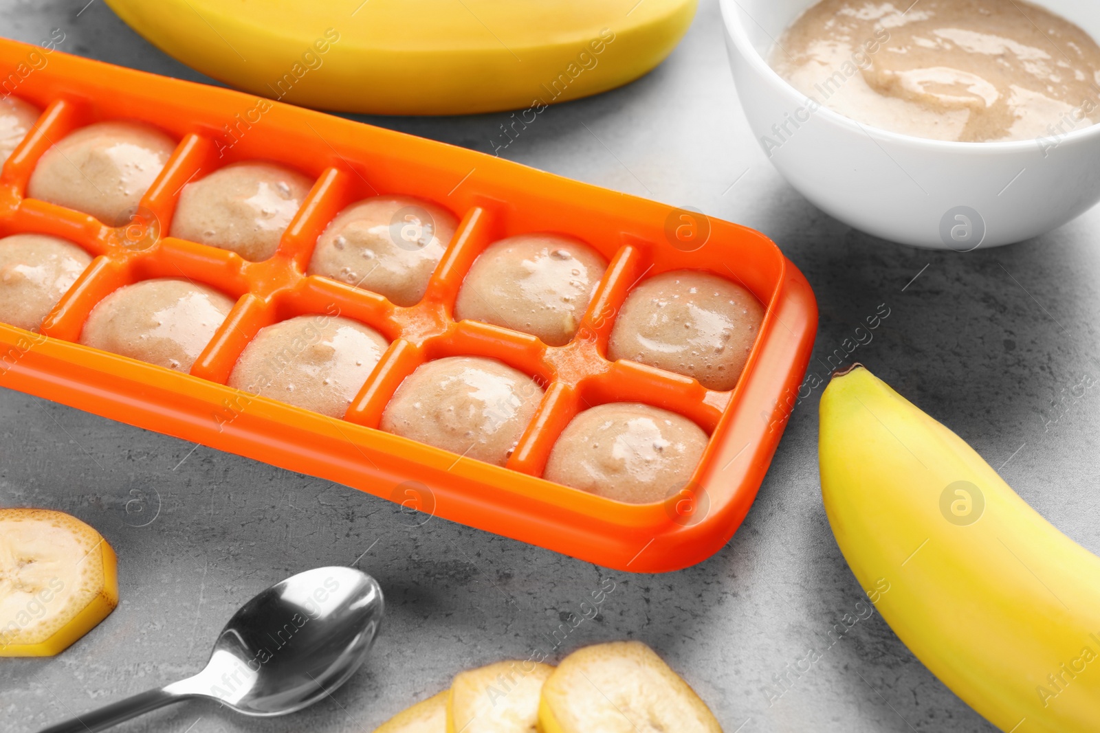 Photo of Banana puree in ice cube tray with fresh banana fruits on grey table. Ready for freezing