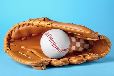Photo of Catcher's mitt and baseball ball on light blue background. Sports game
