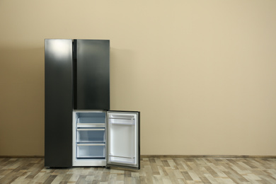 Modern refrigerator near beige wall, space for text