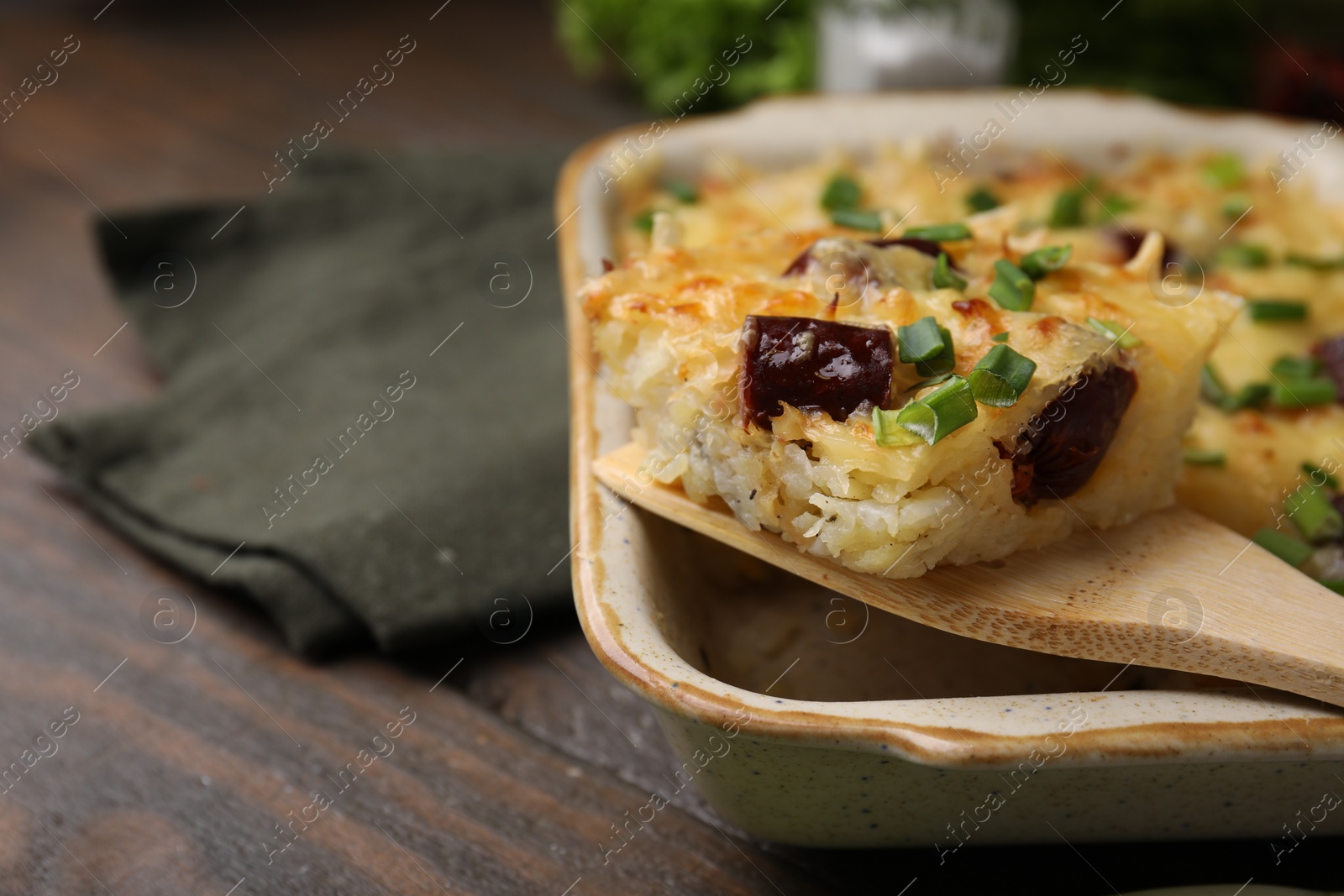 Photo of Taking piece of tasty sausage casserole from baking dish at wooden table, closeup. Space for text