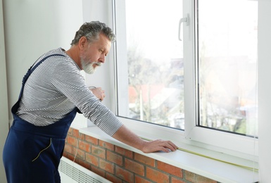 Service man measuring window for installation indoors