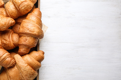 Photo of Tasty fresh croissants on white wooden table, top view. Space for text
