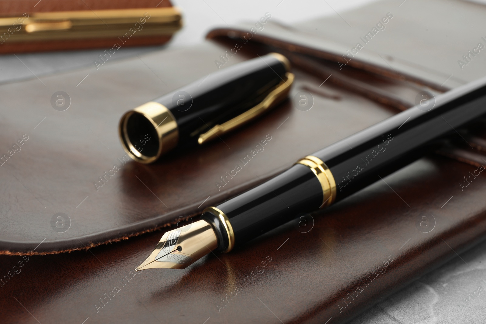 Photo of Stylish fountain pen, cap and leather notebook on light grey table, closeup