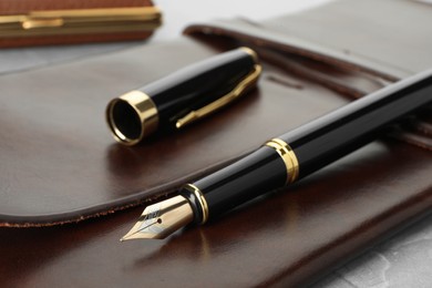 Photo of Stylish fountain pen, cap and leather notebook on light grey table, closeup