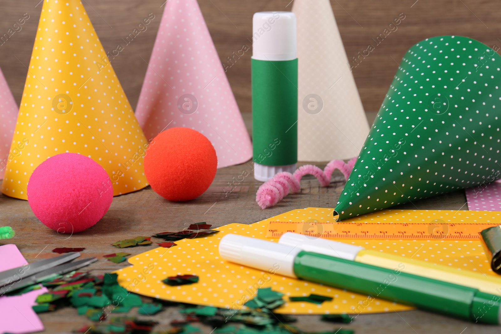 Photo of Different stationery and materials for creation of colorful party hats on wooden table. Handmade decorations