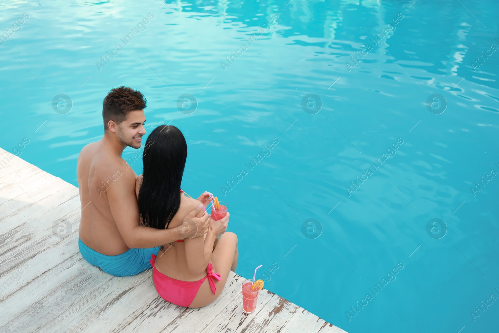 Photo of Woman in bikini with boyfriend near outdoor pool. Happy young couple