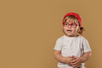 Cute little girl in glasses on pale brown background. Space for text