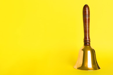 Photo of Golden school bell with wooden handle on yellow background. Space for text