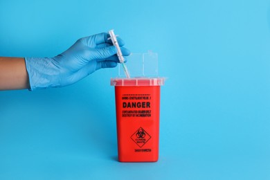 Photo of Doctor throwing used syringe into sharps container on light blue background, closeup