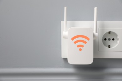 Image of New modern repeater with Wi-Fi symbol plugged into socket on light grey wall, space for text