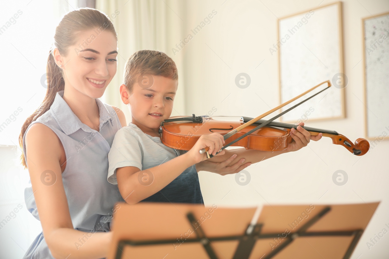 Photo of Young woman teaching little boy to play violin indoors