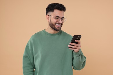 Photo of Happy young man using smartphone on beige background