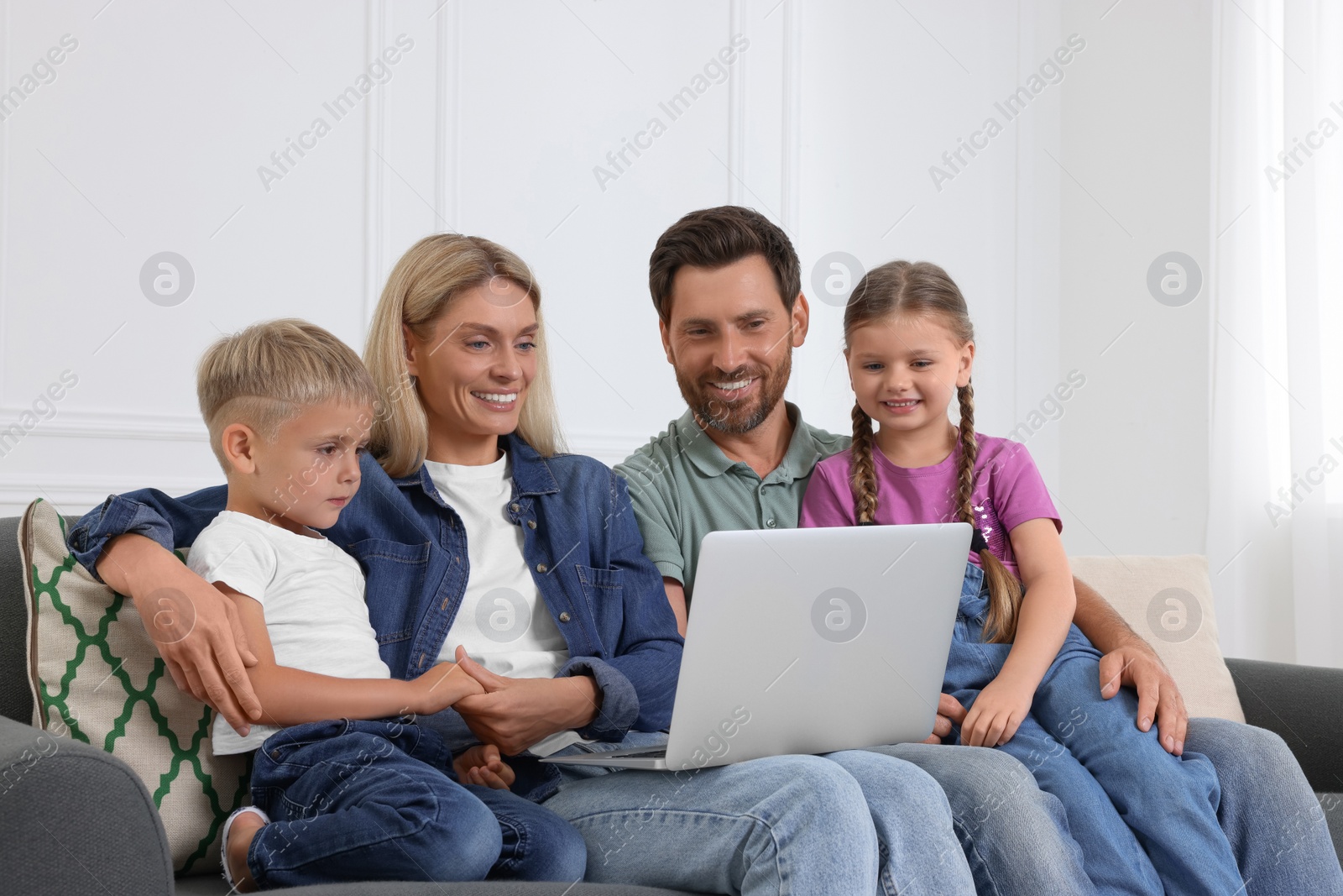 Photo of Happy family with laptop spending time together on sofa at home