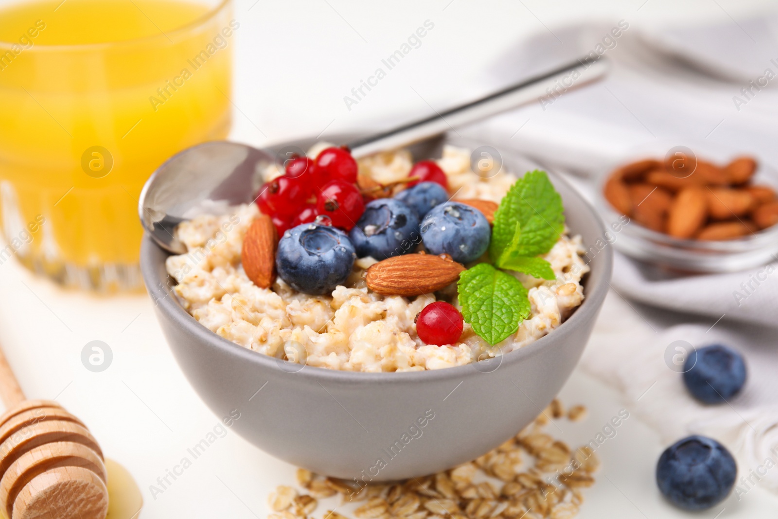Photo of Oatmeal served with berries, almonds and mint on white table, closeup