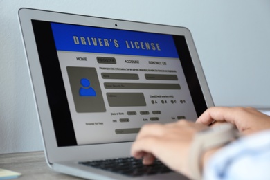 Woman using laptop to fill driver's license application form at table, closeup