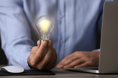 Photo of Glow up your ideas. Closeup view of man holding light bulb while working at wooden desk