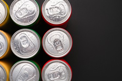 Photo of Energy drinks in wet cans on dark background, top view. Space for text