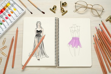 Sketches of different clothes in pad on white wooden table. Fashion designer's desk with stationery, flat lay