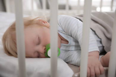 Photo of Cute little baby with pacifier sleeping in crib. Bedtime