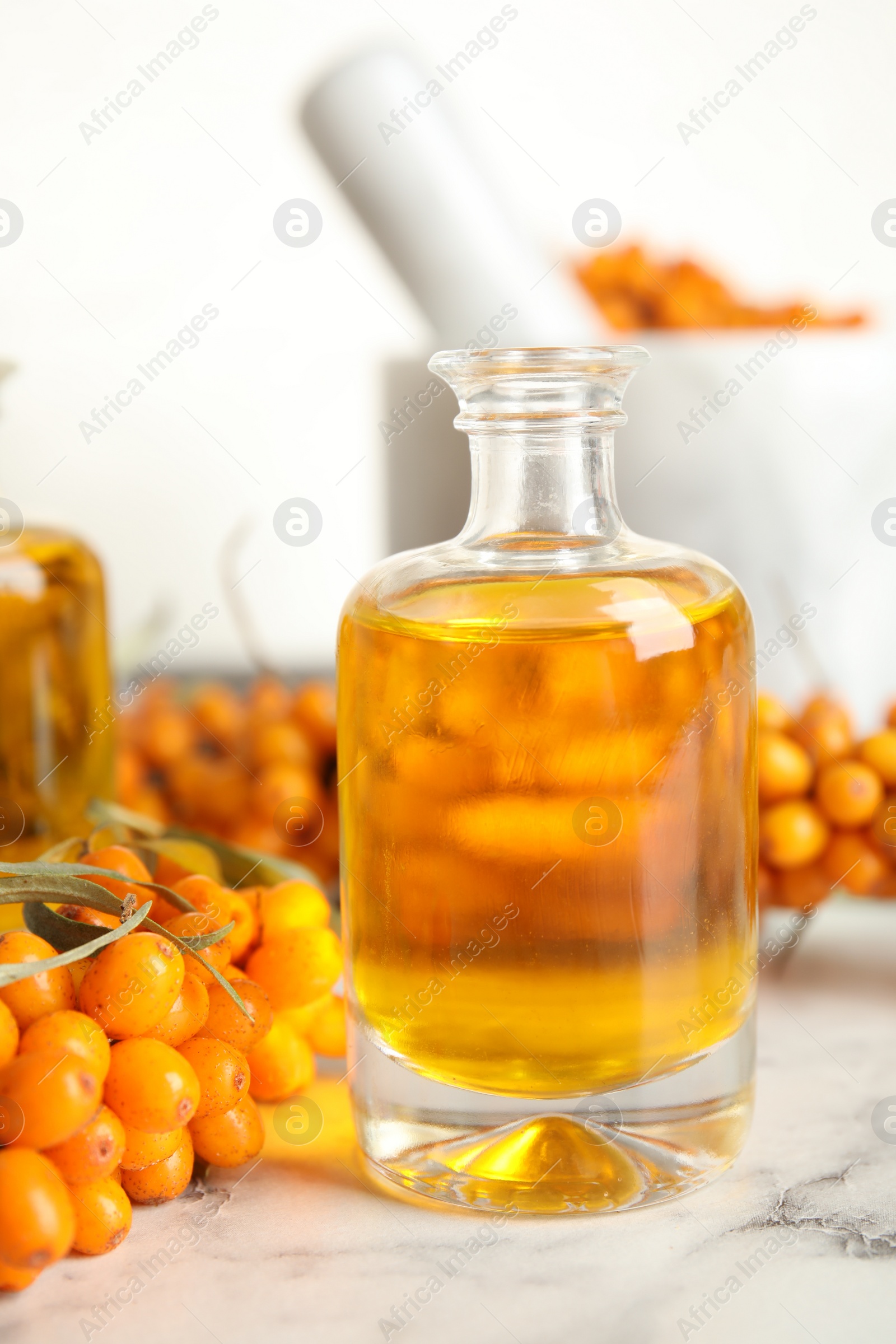 Photo of Natural sea buckthorn oil and fresh berries on white marble table