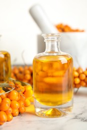 Natural sea buckthorn oil and fresh berries on white marble table