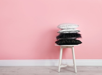 Photo of Many different pillows on chair near color wall with space for text