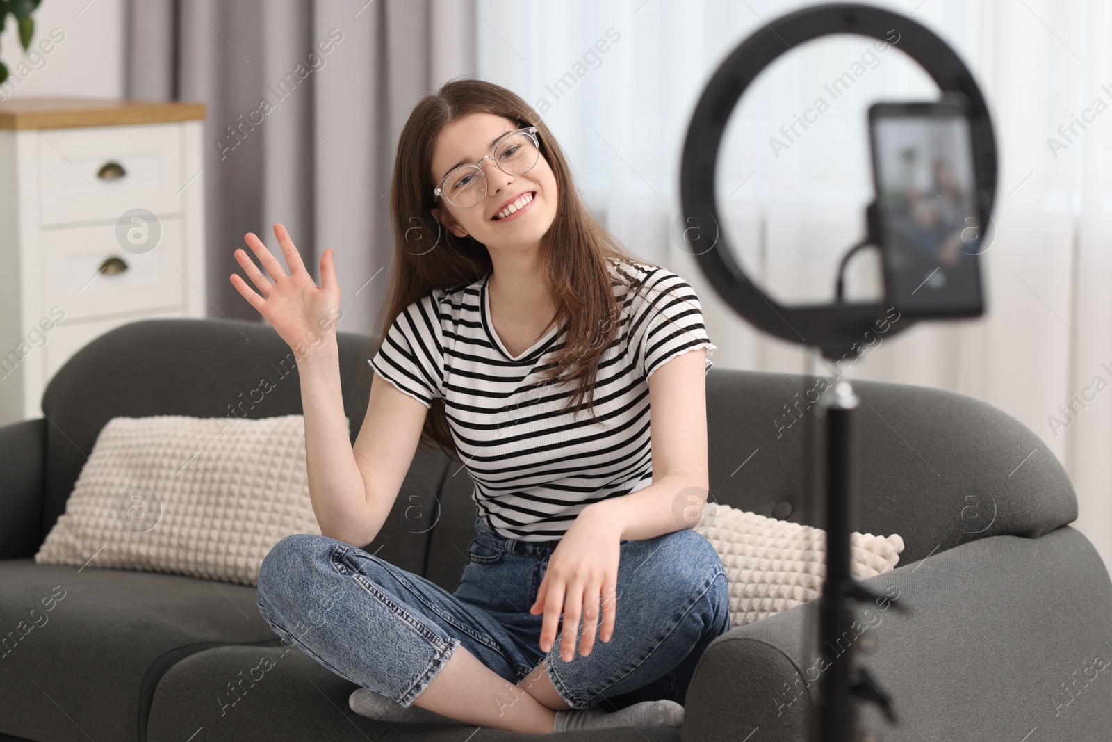 Photo of Smiling teenage blogger waving hello to her subscribers while streaming at home