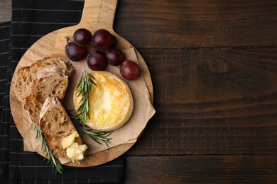 Photo of Tasty baked camembert, pieces of bread, grapes and rosemary on wooden table, top view. Space for text