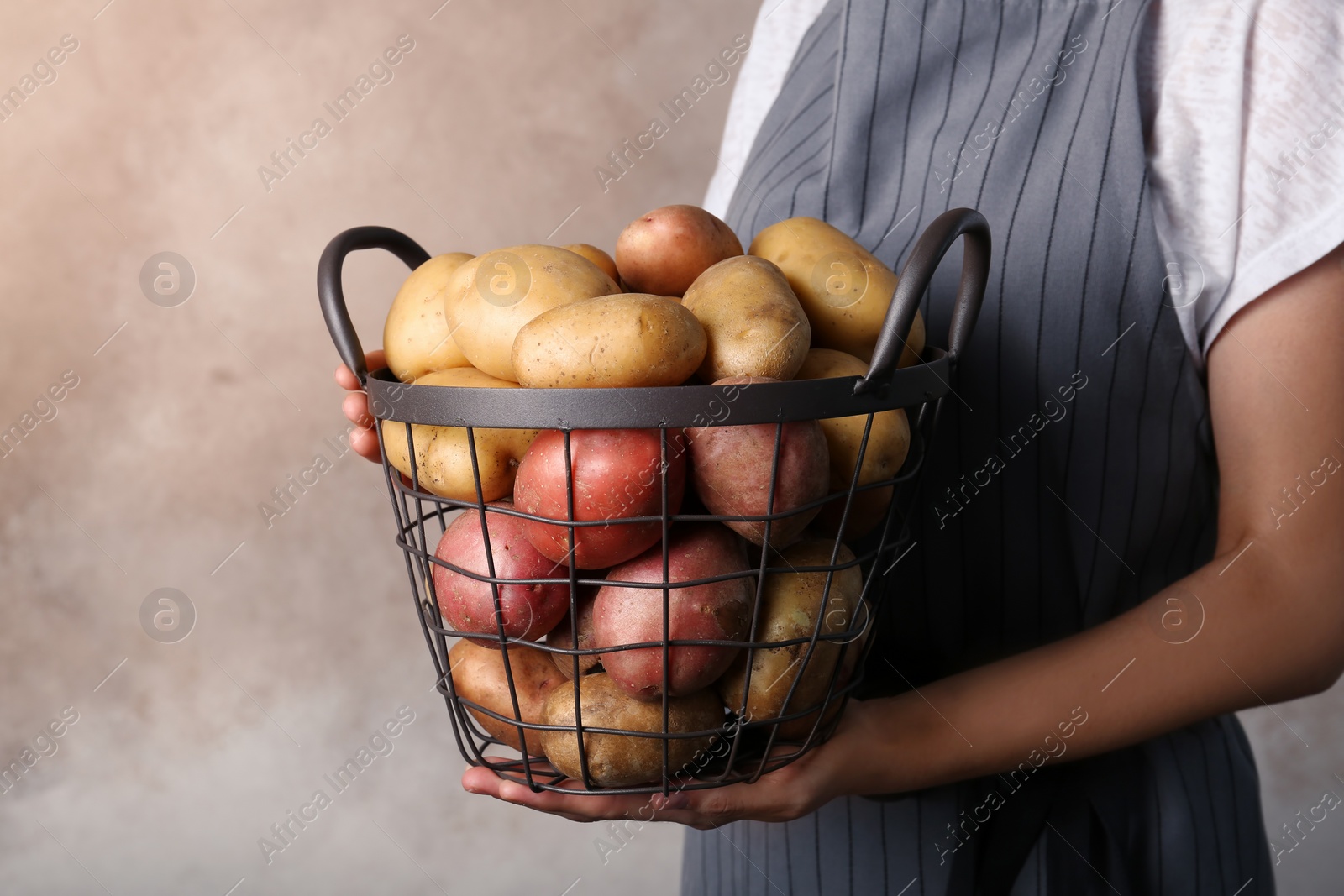 Photo of Person holding basket with fresh organic potatoes on color background