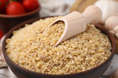 Photo of Bowl and scoop with raw bulgur on table, closeup