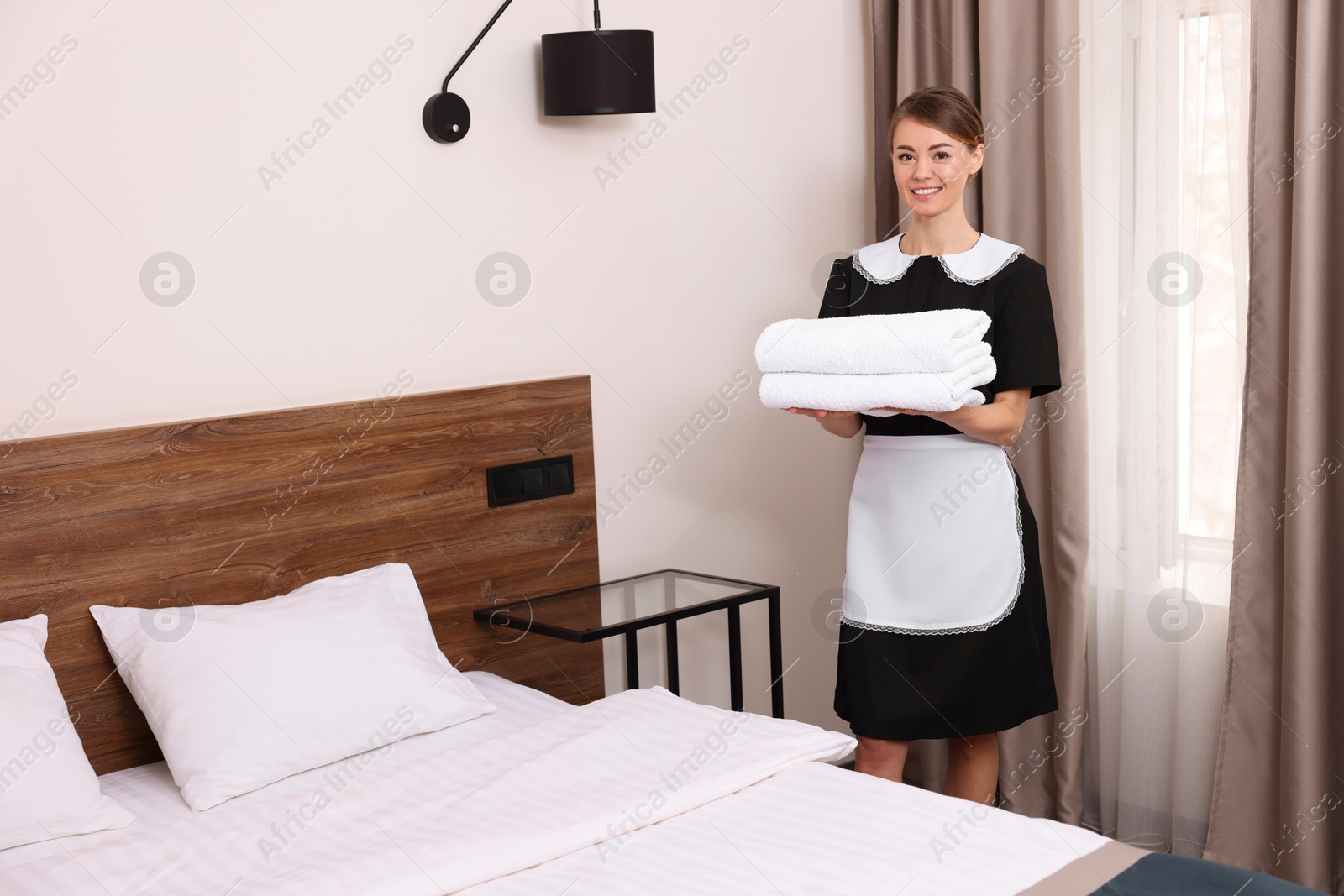 Photo of Beautiful chambermaid with stack of fresh towels in hotel room